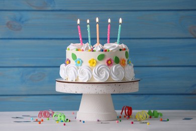 Delicious birthday cake and party decor on white wooden table against light blue background