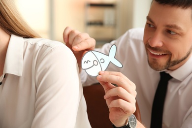 Man sticking paper fish to colleague's back in office. Funny joke