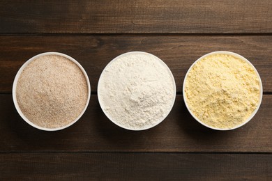 Different types of flours on bowls on wooden table, flat lay