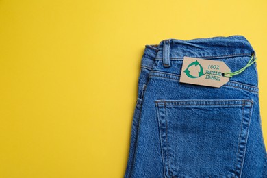 Jeans with recycling label on yellow background, top view. Space for text