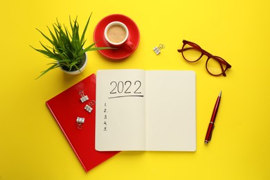 Flat lay composition with open planner on yellow background. 2022 New Year aims