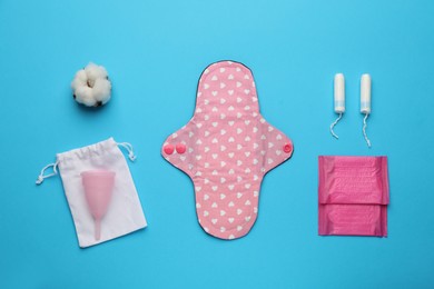Cloth menstrual pad near other reusable and disposable female hygiene products on light blue background, flat lay