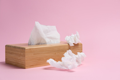 Holder with paper tissues and used crumpled napkins on pink background