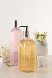 Liquid soap in stylish dispenser, bottle of shower gel and cream on white table
