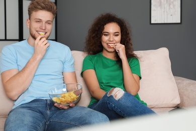 Photo of Young couple with snack and video game controller on sofa indoors