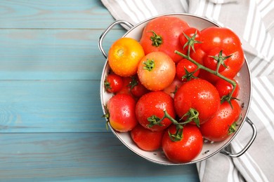 Many different ripe tomatoes in colander on light blue wooden table, top view. Space for text