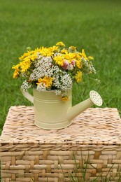 Photo of Pale yellow watering can with beautiful flowers on wicker box outdoors