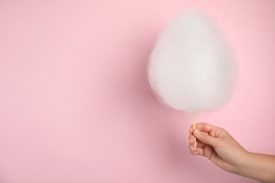 Photo of Woman holding sweet cotton candy on pink background, closeup view. Space for text
