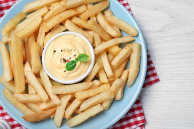 Delicious French fries and cheese sauce on white wooden table