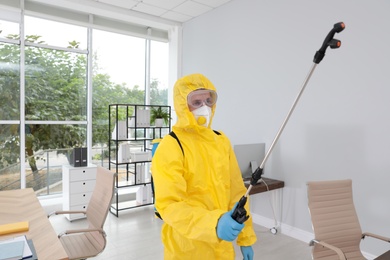 Janitor in protective suit disinfecting office to prevent spreading of COVID-19