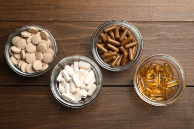 Photo of Different dietary supplements in glass bowls on wooden table, flat lay