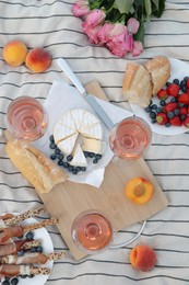Glasses of delicious rose wine, flowers and food on white picnic blanket, flat lay