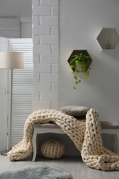 Indoor bench with soft chunky knit blanket, cushion and pouf in room. Interior design