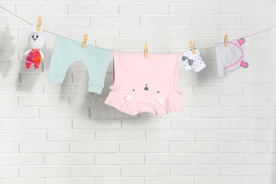 Baby clothes hanging on washing line near white brick wall