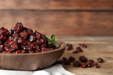 Dried cranberries in bowl on wooden table, closeup. Space for text