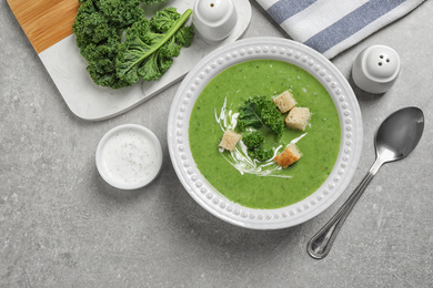 Tasty kale soup with croutons served on grey table, flat lay