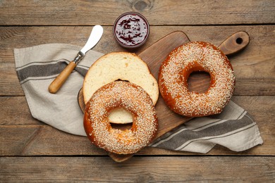 Delicious fresh bagels with sesame seeds and jam on wooden table, flat lay