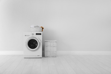 Washing machine with laundry and basket near wall. Space for text