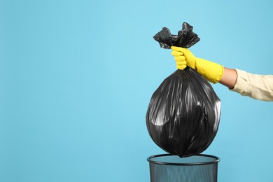 Woman taking garbage bag out of bin on light blue background, closeup. Space for text