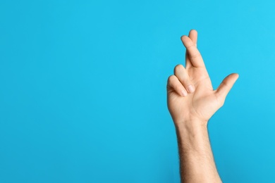 Man with crossed fingers and space for text on light blue background, closeup. Superstition concept