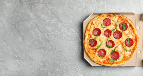 Tasty pepperoni pizza in cardboard box on light grey marble table, top view. Space for text