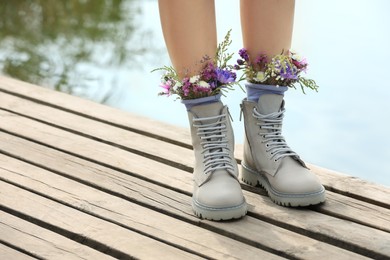 Woman standing on wooden pier with flowers in socks outdoors, closeup. Space for text