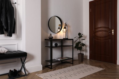 Photo of Console table with decor and mirror on white wall in hallway. Interior design