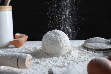 Photo of Sprinkling flour over dough at table against black background