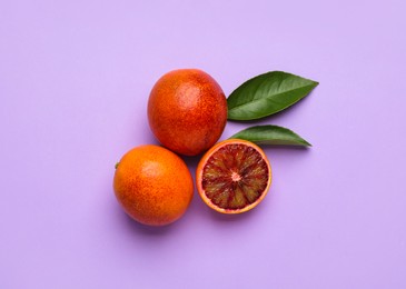Ripe sicilian oranges and leaves on violet background, flat lay