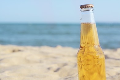Photo of Bottle of cold beer on beach near sea, closeup. Space for text