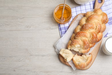 Broken homemade braided bread, milk with honey on white wooden table, flat lay and space for text. Traditional Shabbat challah