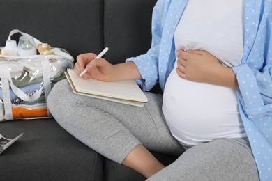 Pregnant woman preparing list of necessary items to bring into maternity hospital at home, closeup
