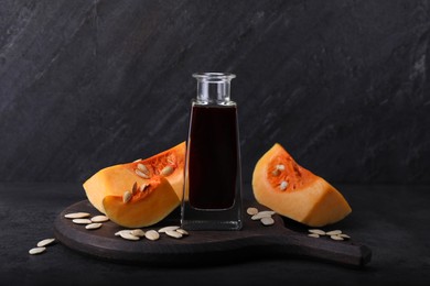Photo of Fresh pumpkin seed oil in glass bottle on dark grey table