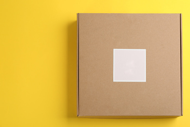 Closed cardboard box on yellow background, top view. Space for text