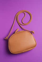 Photo of Stylish leather handbag on purple background, top view