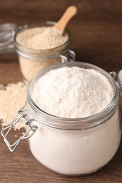Photo of Jars with quinoa flour and seeds on wooden table, closeup