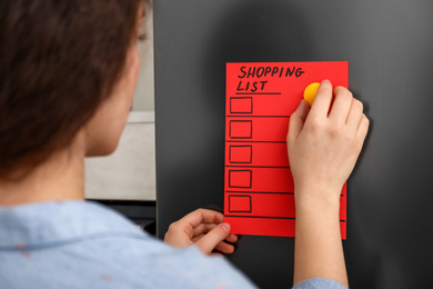 Woman putting shopping list on refrigerator door, closeup