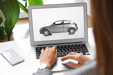 Photo of Woman using laptop to buy car at table indoors, closeup