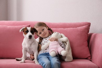 Cute little girl with her dog and toy bunny on sofa indoors. Childhood pet