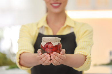 Woman holding jar of pickled vegetables in kitchen, closeup