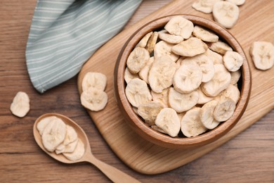 Bowl and spoon with dried banana slices on wooden table, flat lay