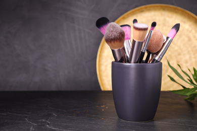 Set of professional makeup brushes in holder on black table. Space for text