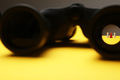 Photo of Recruiter searching employee. Red and white pawns visible through binoculars on yellow background
