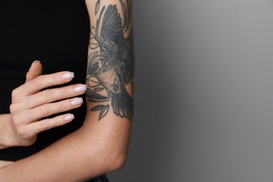 Woman applying cream on her arm with tattoos against light grey background, closeup