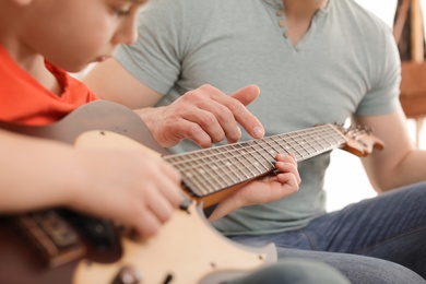 Little boy playing guitar with his teacher at music lesson, closeup. Learning notes