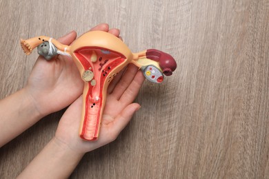 Woman with anatomical model of uterus at wooden table, top view and space for text. Gynecology concept