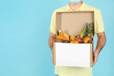 Courier holding box with assortment of exotic fruits on turquoise background, closeup. Space for text