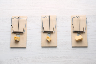 Mousetraps with pieces of cheese on white wooden background, flat lay. Pest control