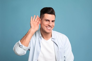 Man showing hand to ear gesture on light blue background