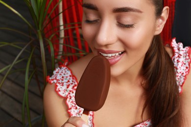 Beautiful young woman eating ice cream glazed in chocolate on city street, closeup